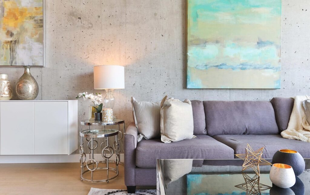 Sala con sillon gris, lampara y mesas de cristal con una pared gris y un cuadro en la pared